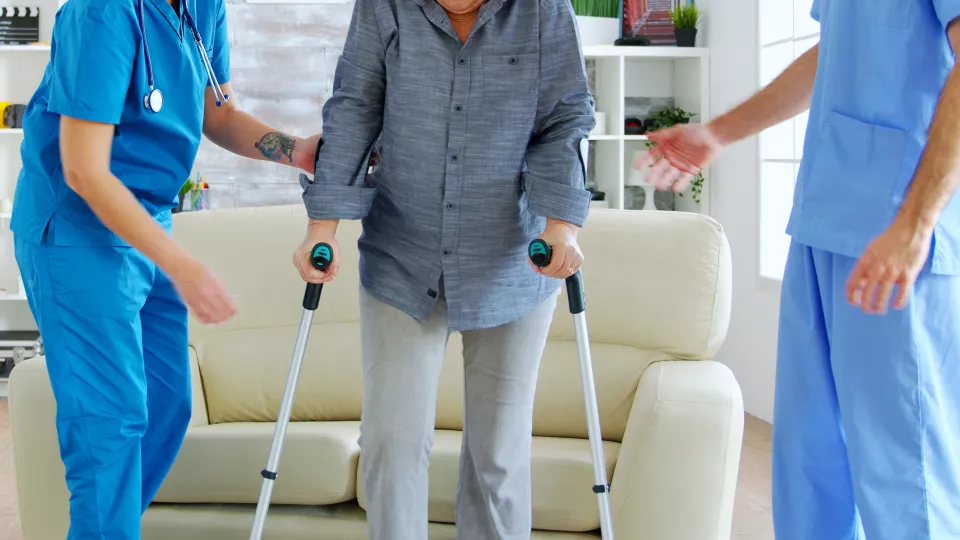 En äldre person på kryckor får hjälp av vårdpersonal.