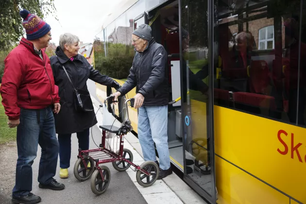 Tre äldre personer vid en busshållsplats. Foto.