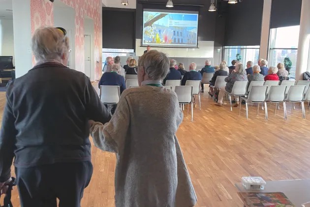 Äldre går fram mot stolar i föreläsningssal